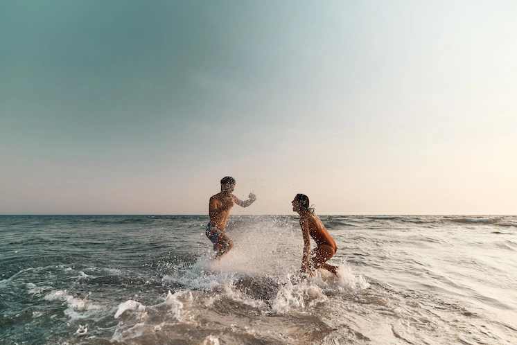 Playful couple splashing in the ocean at sunset, embracing adventure and relaxation on the Outer Banks.