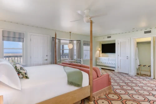 Spacious room with a king-size bed, surrounded by windows offering sea views, and a carpet with geometric patterns.