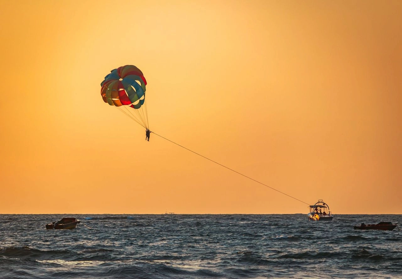 A person soaring through the sky while parasailing, embracing the thrill against a breathtaking, fiery orange sunset.