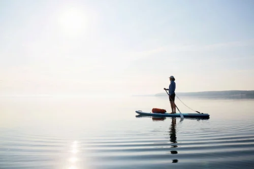 A woman peacefully practicing paddleboarding, enjoying the calm waters, thanks to the convenient Water Sport Rentals available.