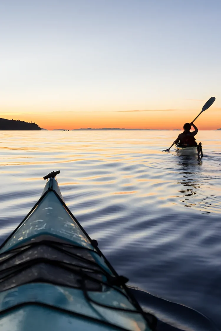 Two people kayaking at sunset near The Sanderling Hotel, enjoying a peaceful coastal adventure