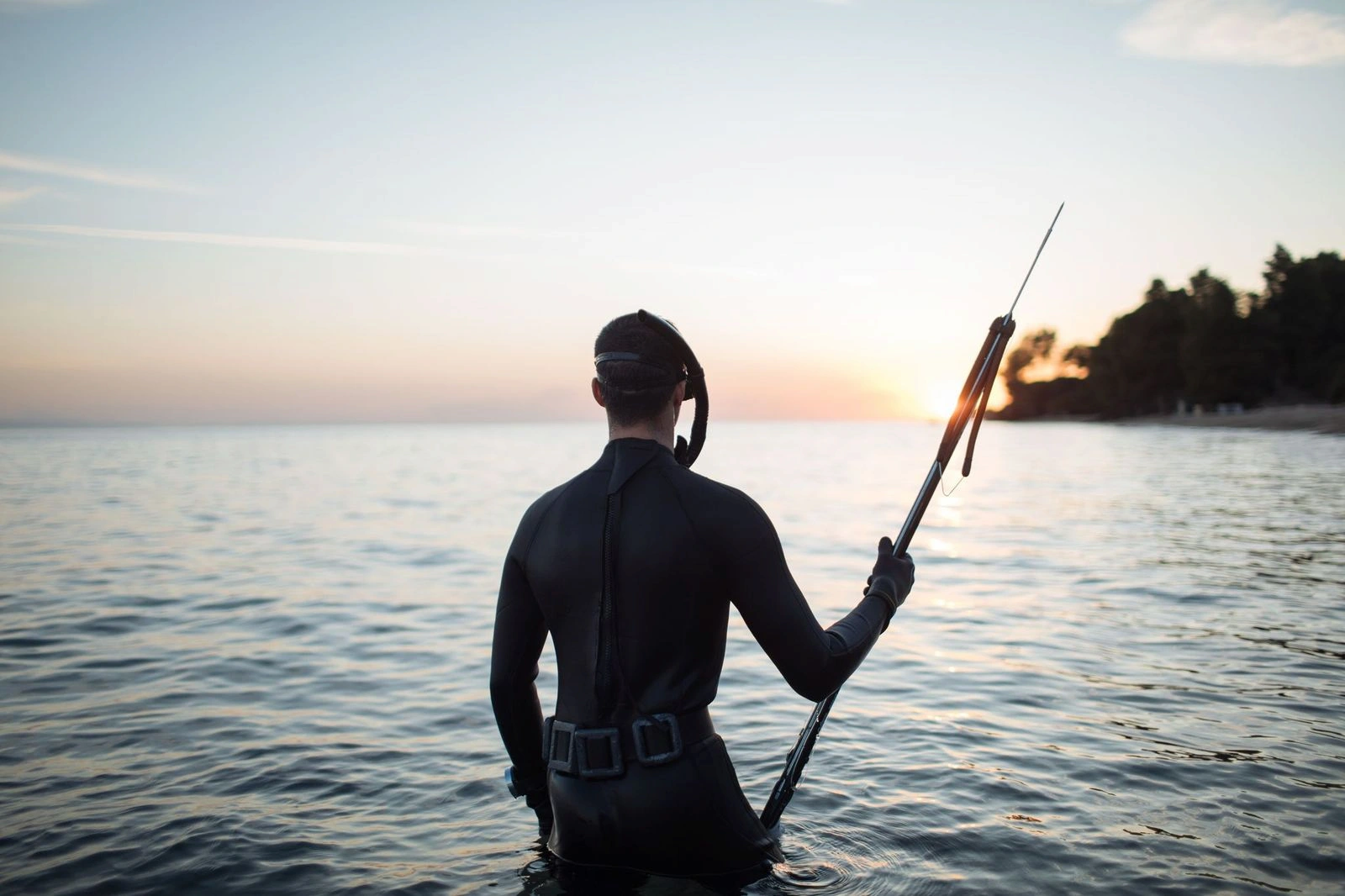 A man on the beach, fully equipped in a wetsuit and gear, ready for an exciting spearfishing adventure.