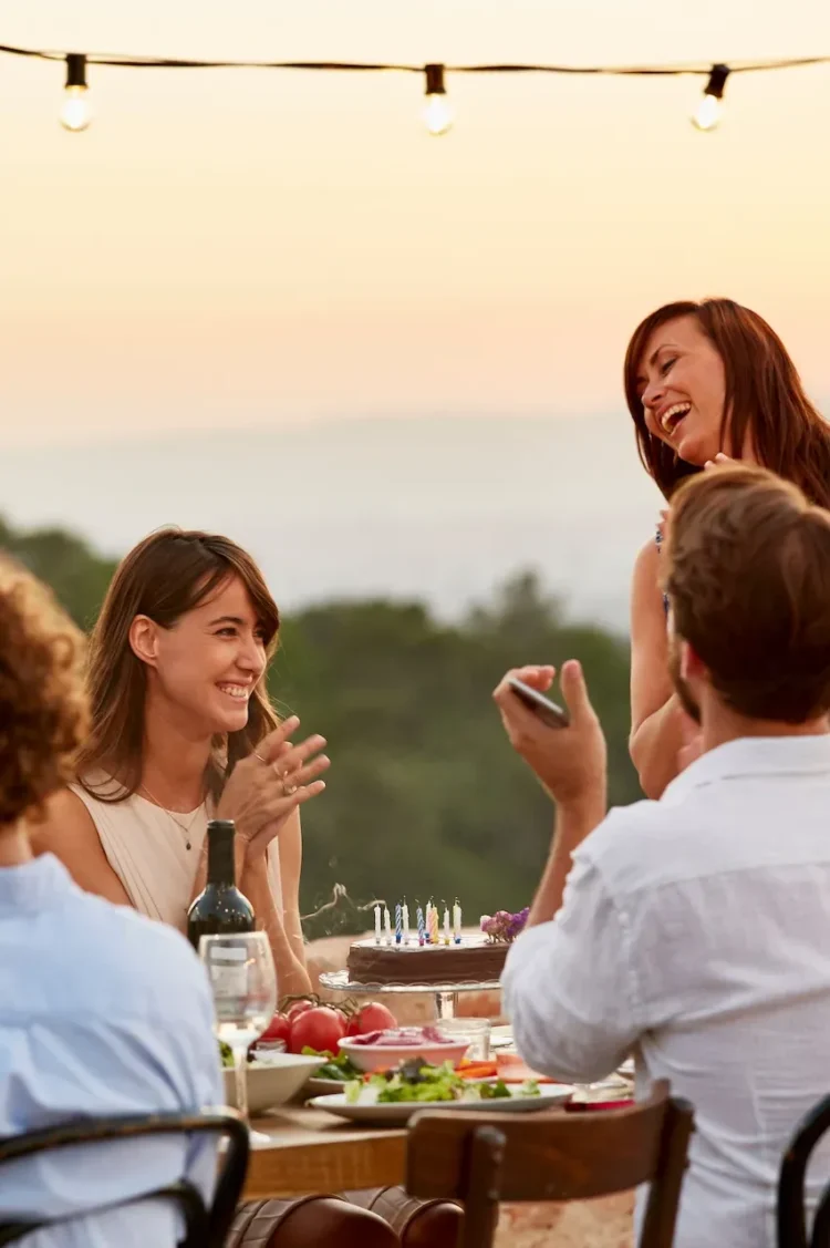 Friends celebrating a birthday with food and drinks at sunset at The Sanderling Hotel – joyful outdoor gathering.