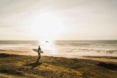 A man gazing at the ocean, reflecting on his surf lesson, with the waves gently rolling in the background.