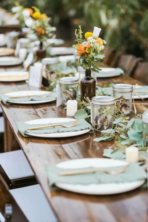 Beautiful long dark wood table decorated with pastel green details, a vibrant orange floral centerpiece, and gold cutlery.