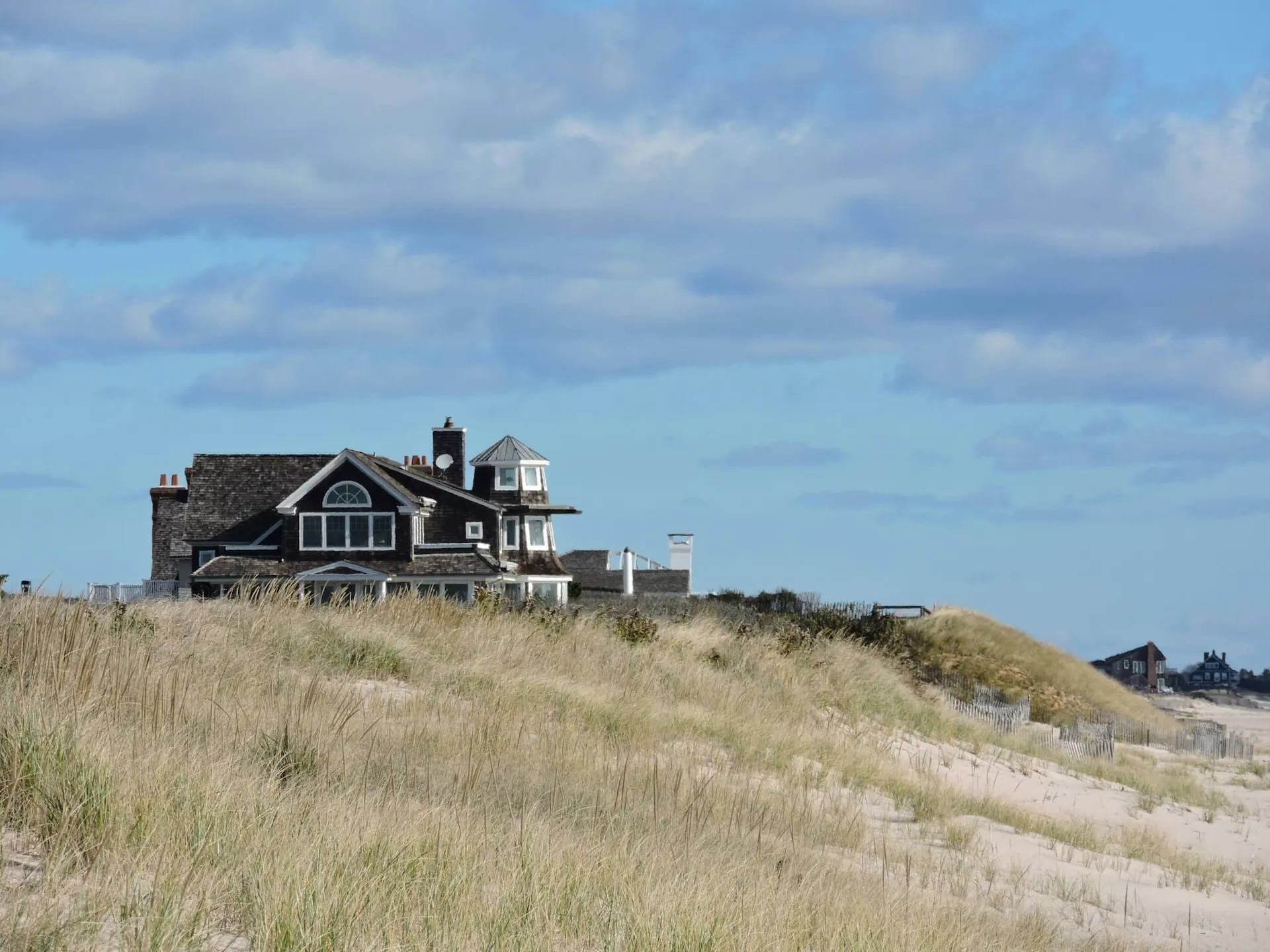 Distant view of one of The Sanderling Resort residences by the beach, behind the dunes, under a beautiful blue sky.