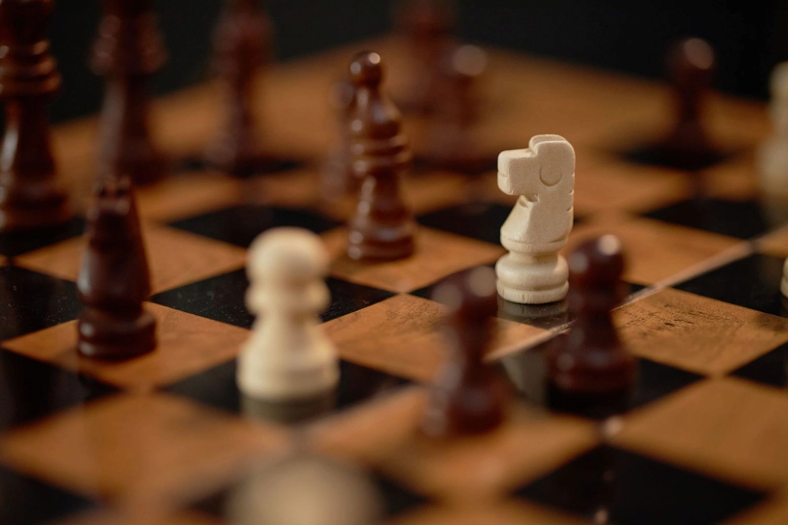 Close-up of a chessboard with wooden and black squares, showing chess pieces in mid-game.