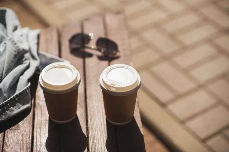 Two to-go coffee cups resting on a wooden bench, ready for a cozy stroll.