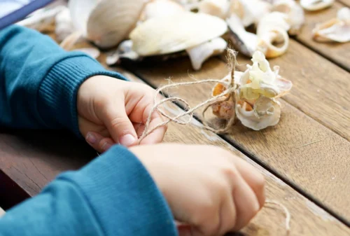 A child joyfully crafting with beach shells on a rustic wooden table.